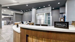 Zona de recepción de un hotel con un mostrador curvo, un cartel que dice "Hilton Honors" y un diseño interior moderno con paredes grises e iluminación empotrada en el techo.