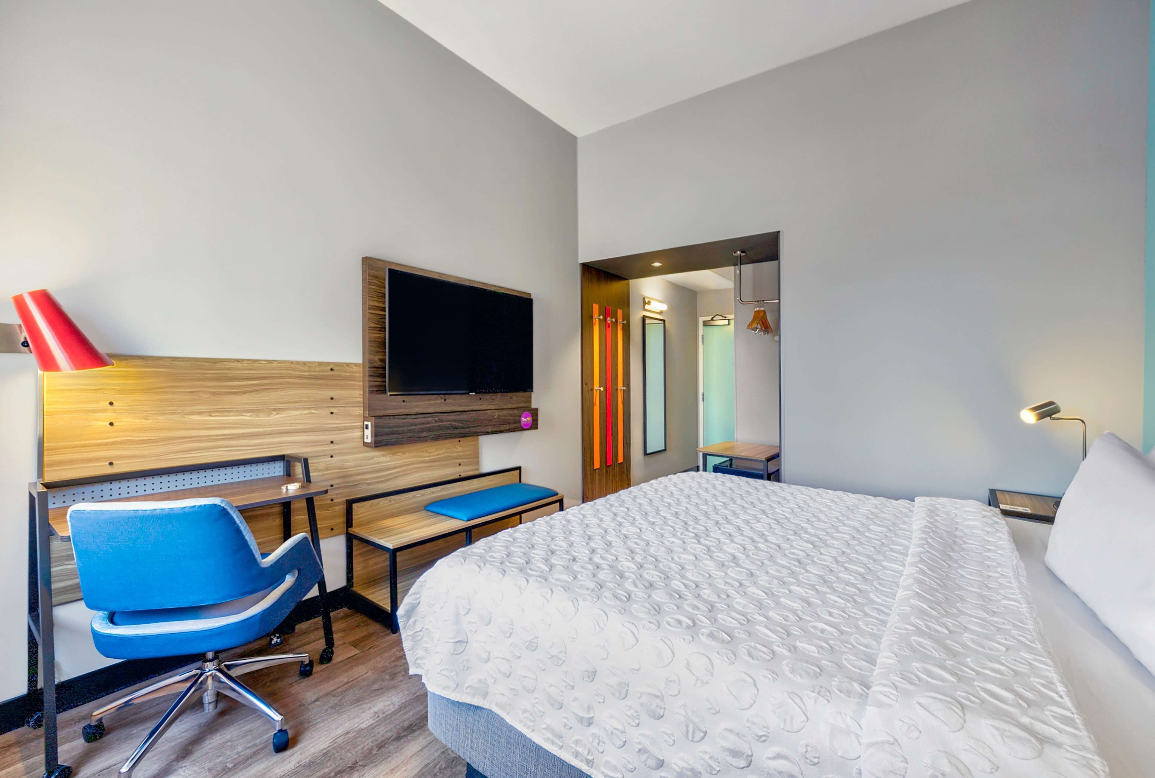 Une chambre d’hôtel moderne avec un grand lit, un bureau, une chaise bleue et un téléviseur fixé au mur.