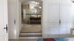 Une chambre avec un lit, une salle de bain avec une douche et un couloir menant à une porte.