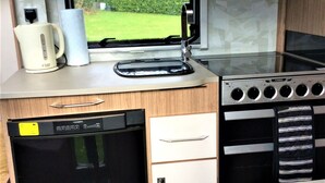 Una kitchenette compacta con lavavajillas, horno, microondas y ventana con vistas a un césped verde.