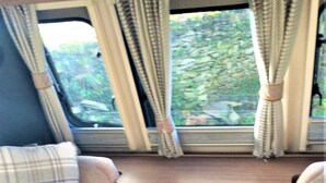 Interior de una caravana compacta, con una cama, un escritorio pequeño con cajones y cortinas.