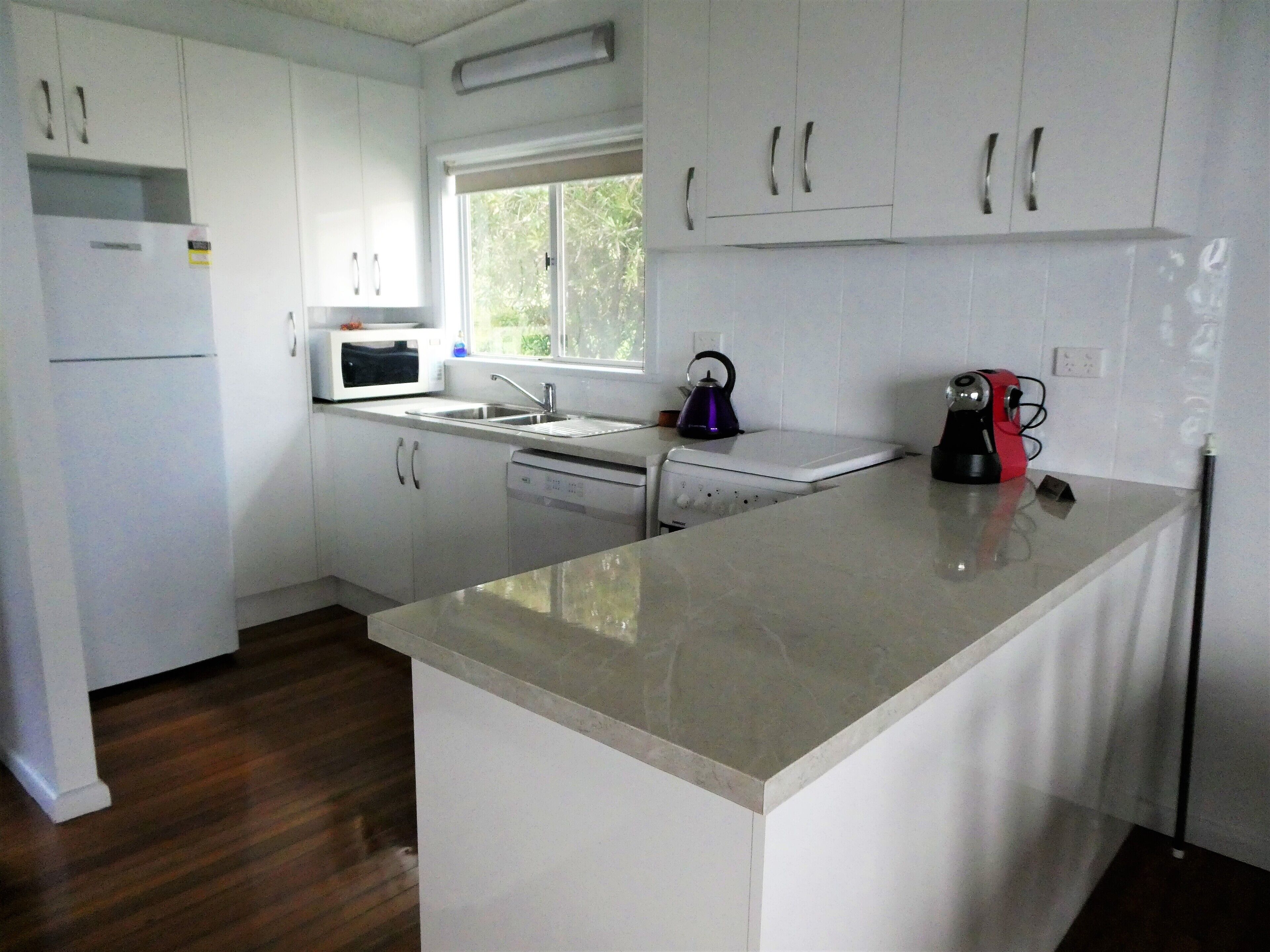 A modern kitchen with white cabinetry, a built-in microwave, a kettle, and a coffee maker.