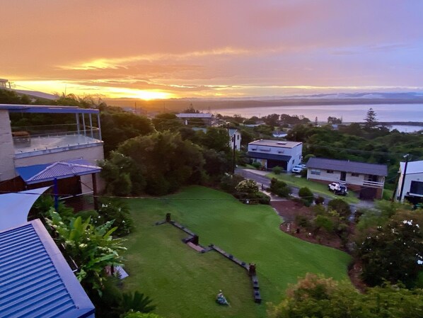 A residential area with houses, a grassy yard, and a view of the sea during sunset.
