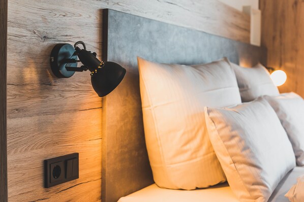 Ein modernes Schlafzimmer mit Holz-Kopfteil, einer Wandlampe und einem Bett mit weißer Bettwäsche.