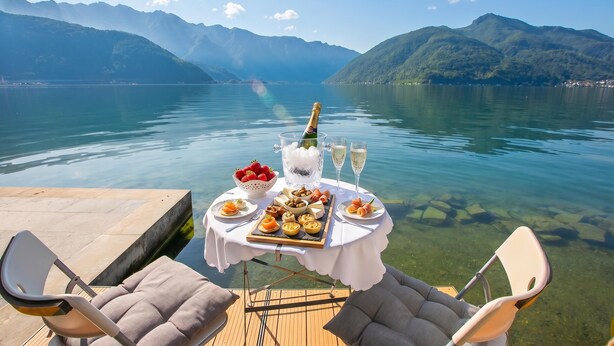 A table set with food and drinks, overlooking a lake with mountains in the background. - Casa Tame - Pieds Dans L'eau (Melide)