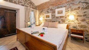 A bedroom with a stone wall, wooden bed, bedside lamps, and a nightstand. - Casa Tame - Pieds Dans L'eau (Melide)