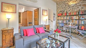 A cozy living room with a grey sofa, red cushions, a coffee table with a teapot, and a bookshelf filled with books. - Casa Tame - Pieds Dans L'eau (Melide)