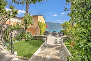 A residential area with a stone staircase, a grassy lawn, and a view of a body of water and mountains. - Casa Tame - Pieds Dans L'eau (Melide)