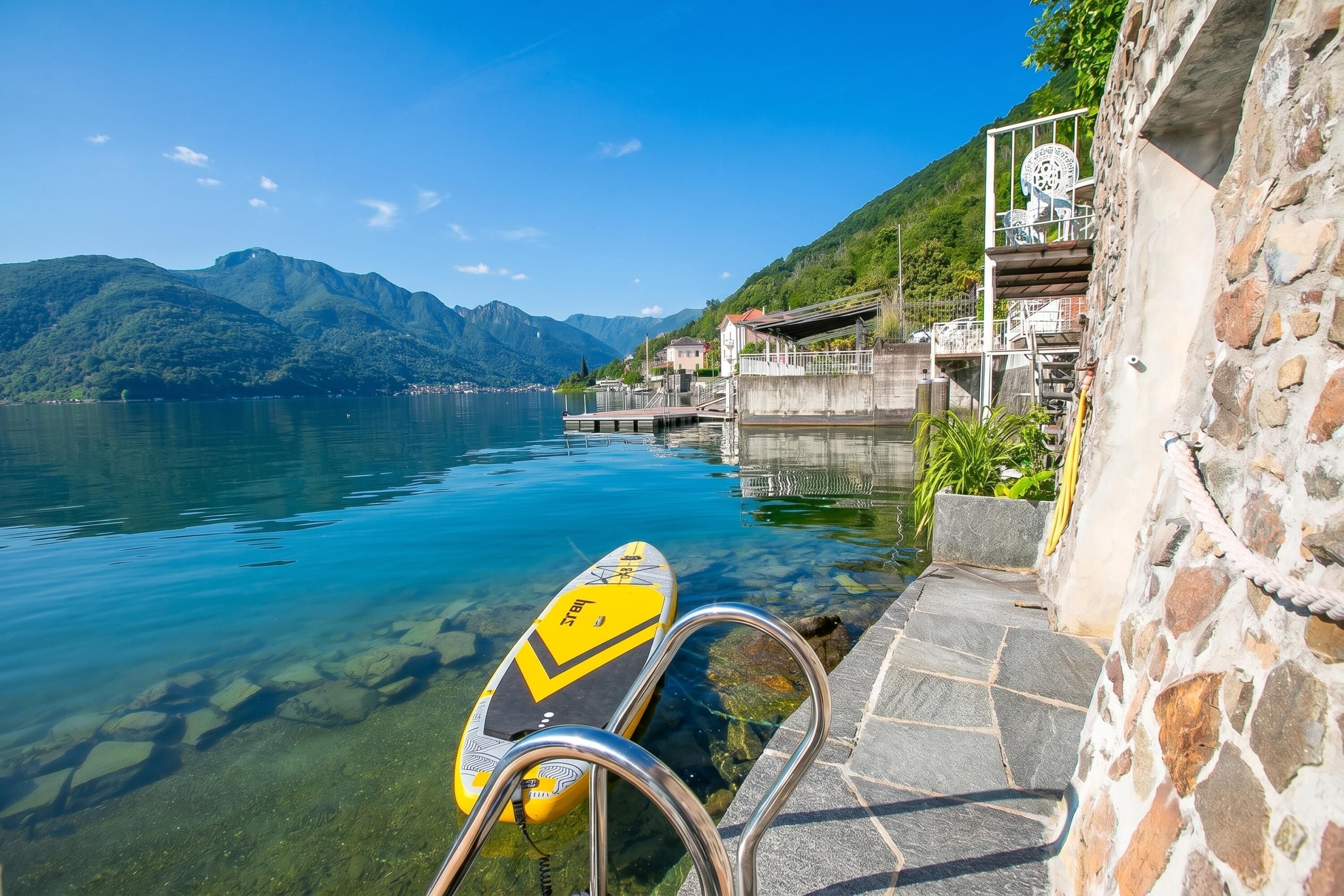 A clear lake with a paddleboard, stone steps, and a mountain backdrop.