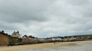 Eine Küstenstadt mit einem markanten, schlossartigen Gebäude, einem Sandstrand und einer hügeligen Landschaft im Hintergrund.