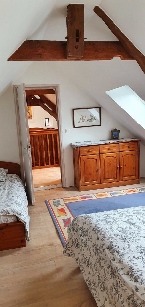 Quarto com teto inclinado, vigas de madeira, cama, cômoda e claraboia.
