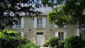 Ein zweistöckiges Steinhaus mit weißen Fensterläden, einem zentralen Eingang und einem gepflegten Garten.