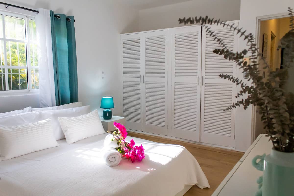A neatly made bed with pillows and a rolled towel, a bedside lamp, and a vase with flowers.