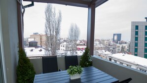 A balcony with a table and chairs, a potted plant, and a view of a cityscape with buildings and bare trees. - Metropole Apartments Old Center (Bucharest)