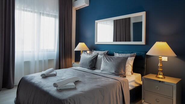 A hotel room with a bed, two bedside tables with lamps, a large mirror, and a window with curtains. - Metropole Apartments Old Center (Bucharest)