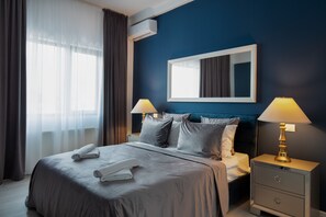 Ein Hotelzimmer mit einem Bett, zwei Nachttischen mit Lampen, einem großen Spiegel und einem Fenster mit Vorhängen.