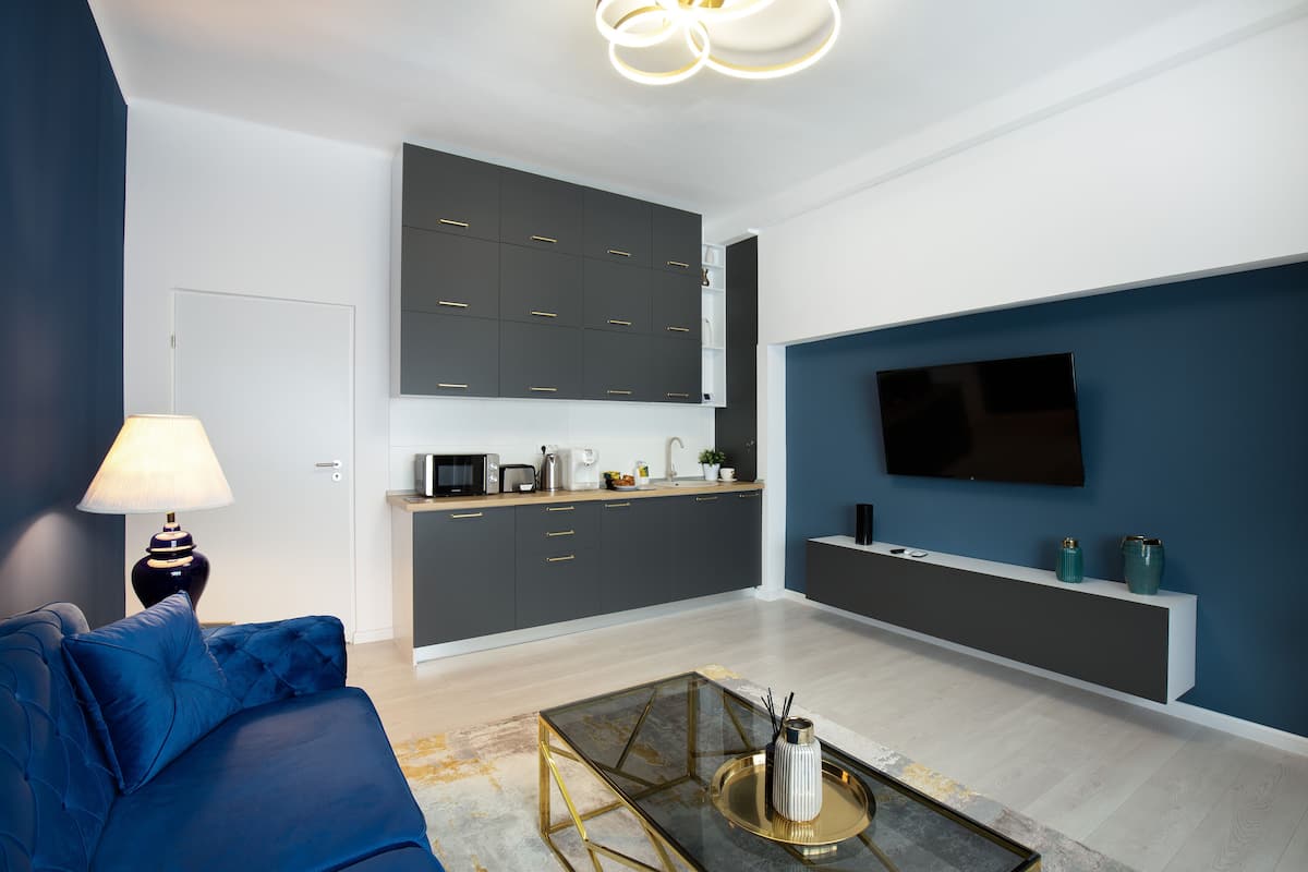 A modern living room with a sofa, a coffee table, a TV, and a kitchen area with cabinets and appliances.