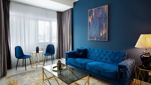 A modern living room with a blue sofa, two chairs, a glass coffee table, and a lamp. - Metropole Apartments Old Center (Bucharest)