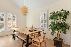 Comedor con mesa de madera, sillas, lámpara colgante y una planta en maceta.