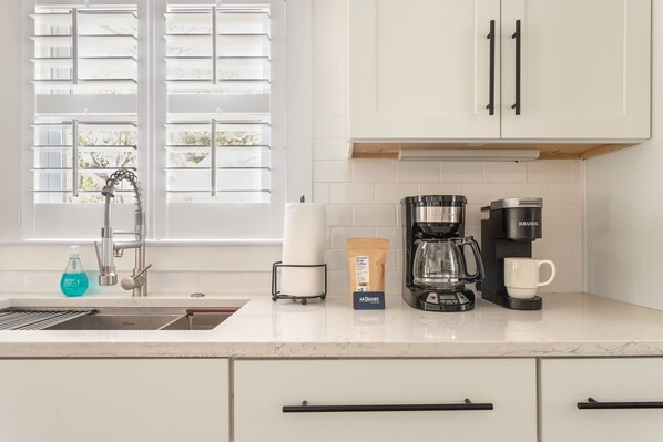 A modern kitchen with white cabinets, a coffee maker, a kettle, and a sink.