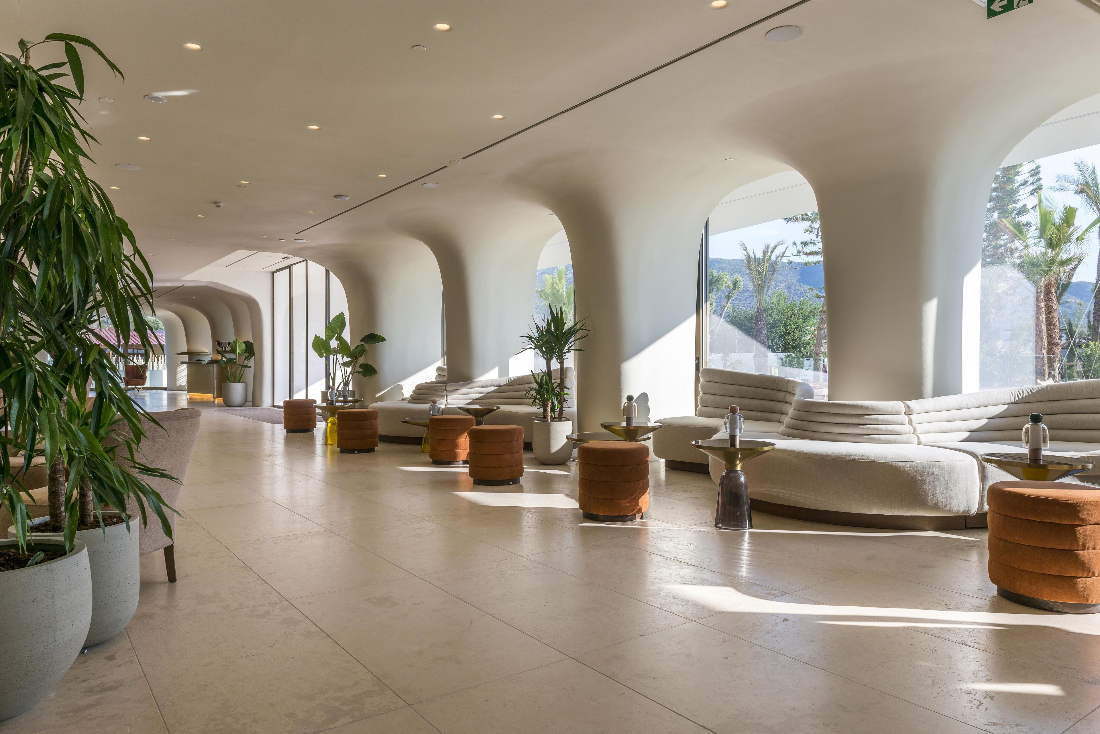 Een ruime lobby met een modern design, met een lange zithoek met banken en poefs, potplanten en uitzicht op het buitengebied.
