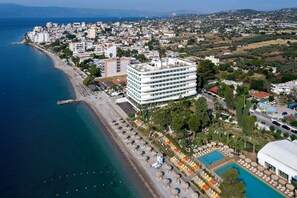 An aerial view of a coastal hotel with a beach, a swimming pool, and a large building with multiple floors. - Isla Brown Corinthia Resort & Spa, Curio Collection Hilton (Loutraki-Agioi Theodoroi)