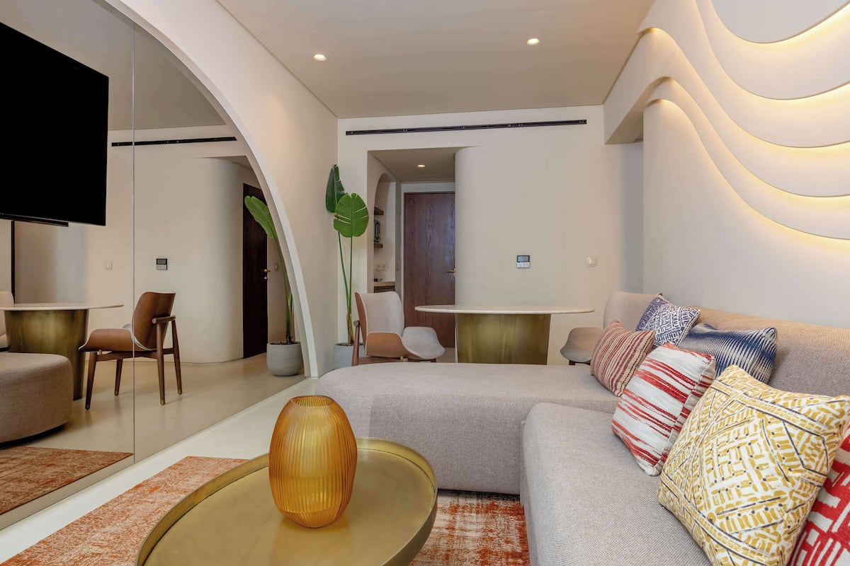 Un salon moderne avec un canapé, une table basse et des coussins décoratifs. Un téléviseur est fixé au mur et une plante se trouve dans un coin.