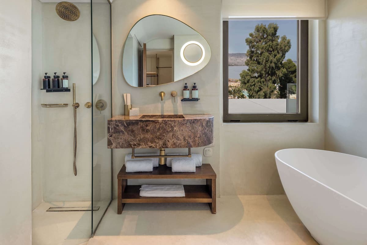 Une salle de bain moderne dotée d’une douche en verre, d’un lavabo en marbre, d’un grand miroir et offrant une vue sur l’extérieur.