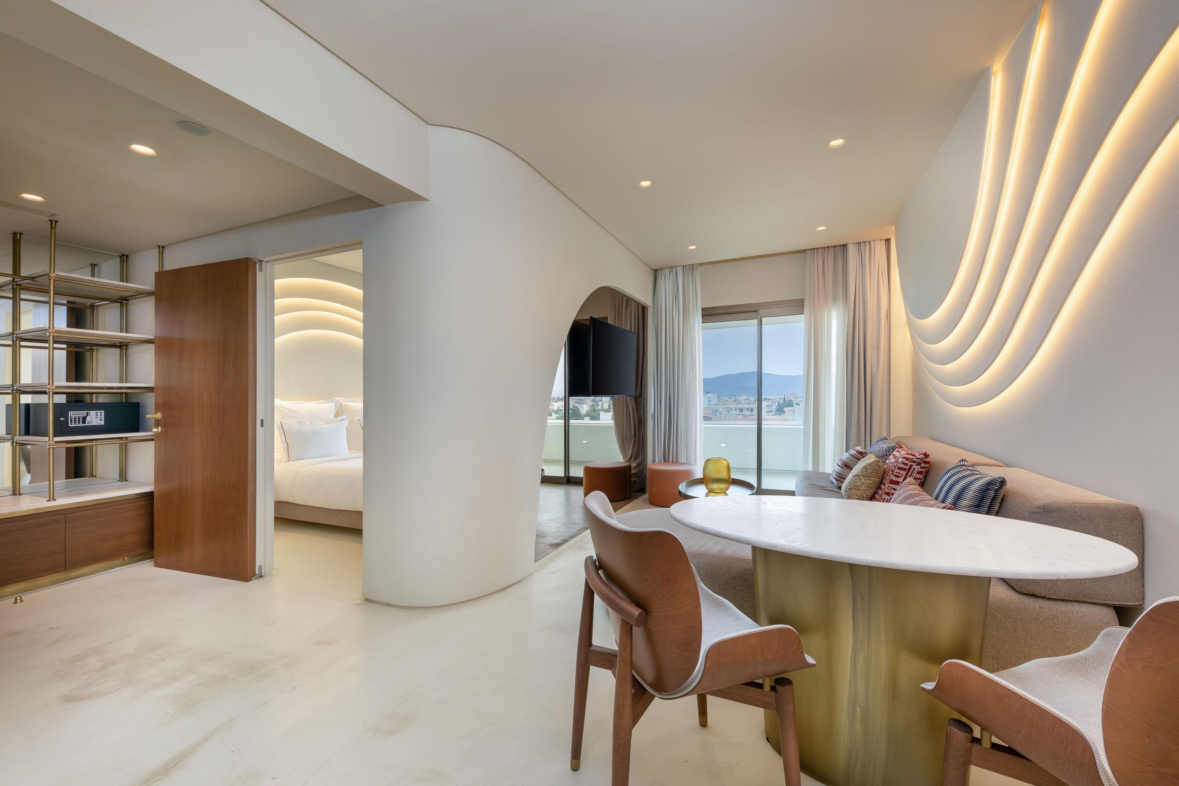 A modern hotel room with a dining area, a sofa, and a view of the cityscape.
