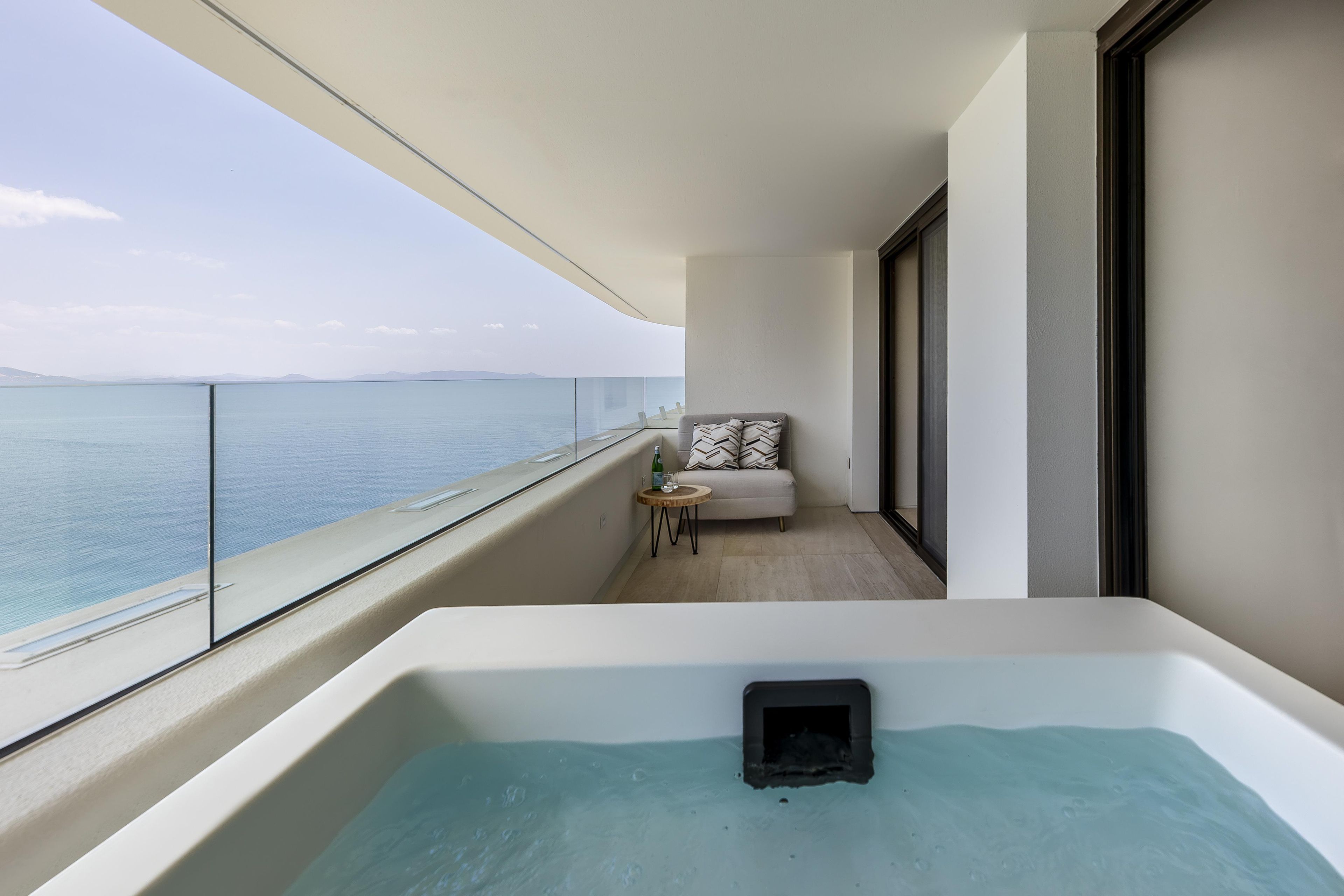 Ein Balkon mit Meerblick, eine Couch, ein kleiner Tisch und eine Whirlwanne.