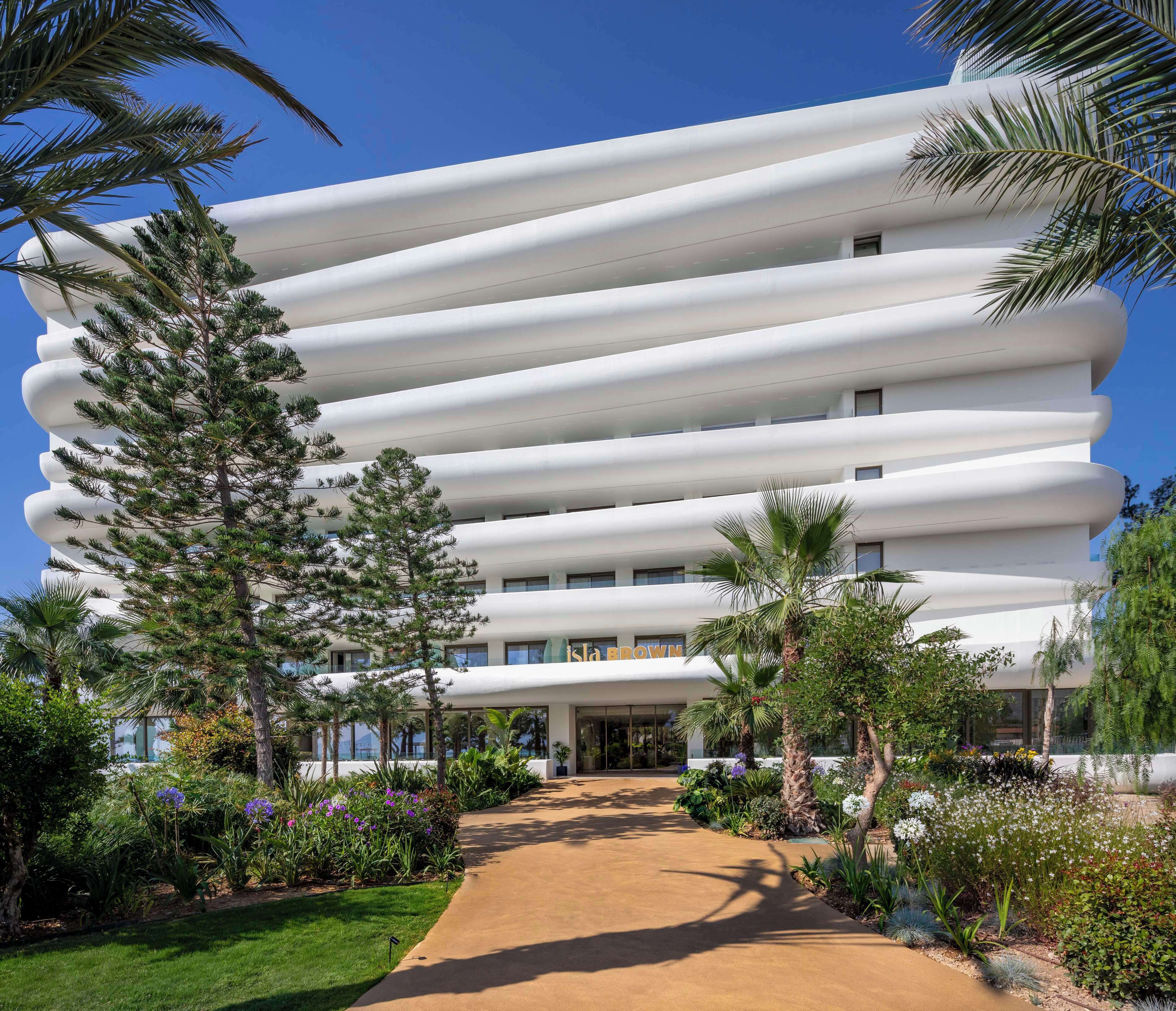 A modern hotel with a unique architectural design featuring horizontal white balconies and a central entrance.