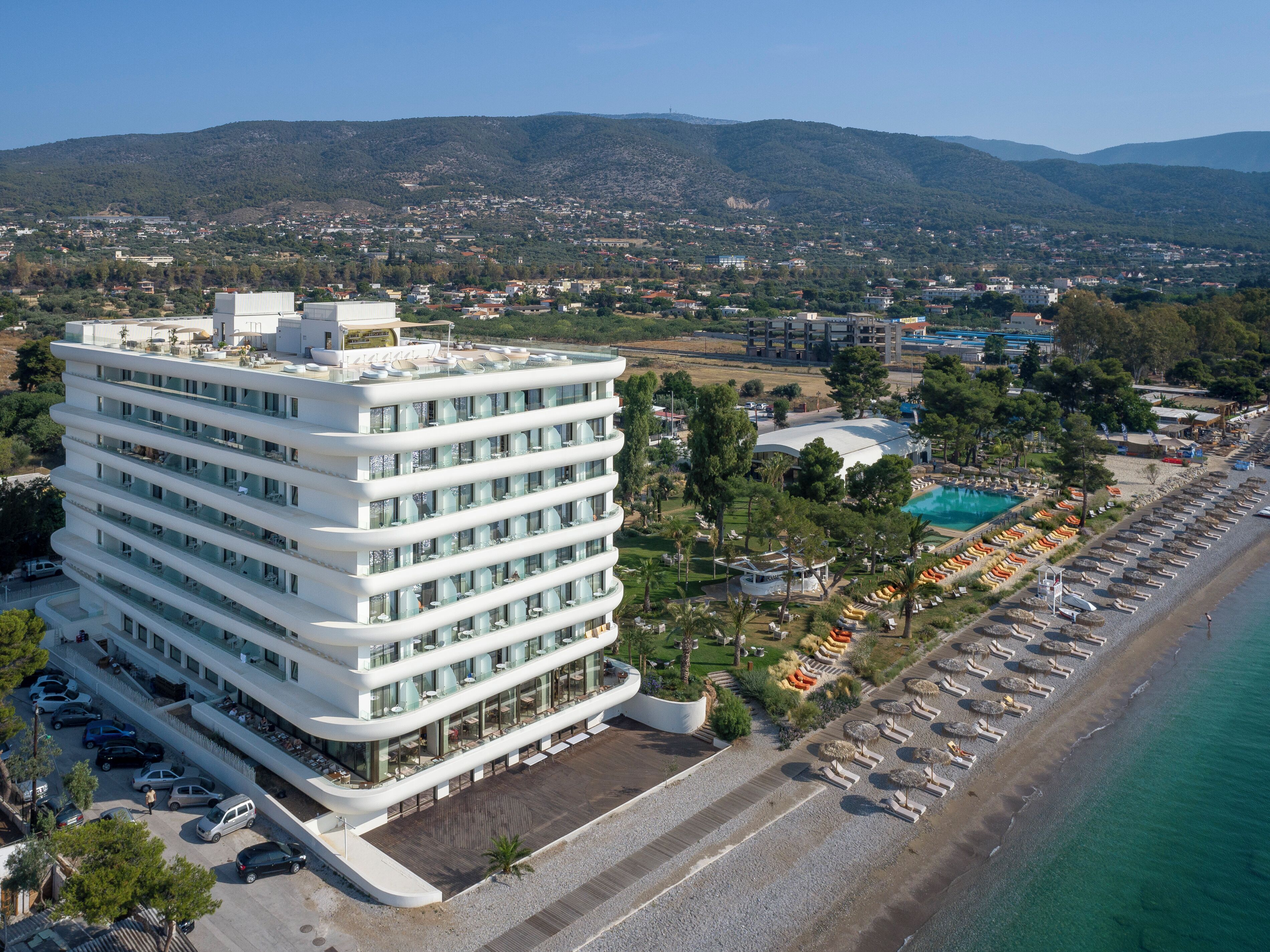 A modern hotel with multiple floors, a rooftop terrace, and a poolside area with sun loungers.