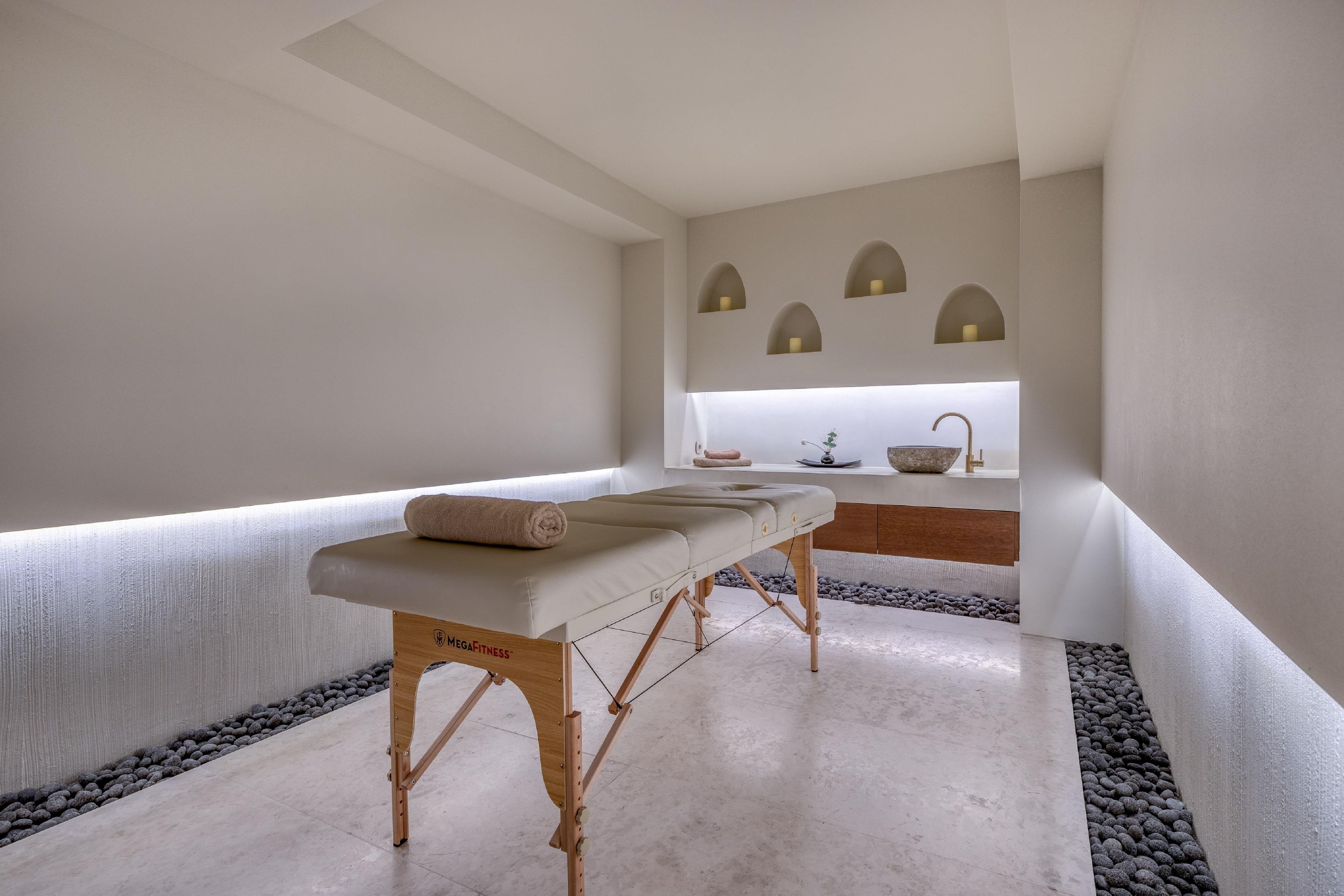 A spa room with a massage table, a small sink, and a window with three lights.