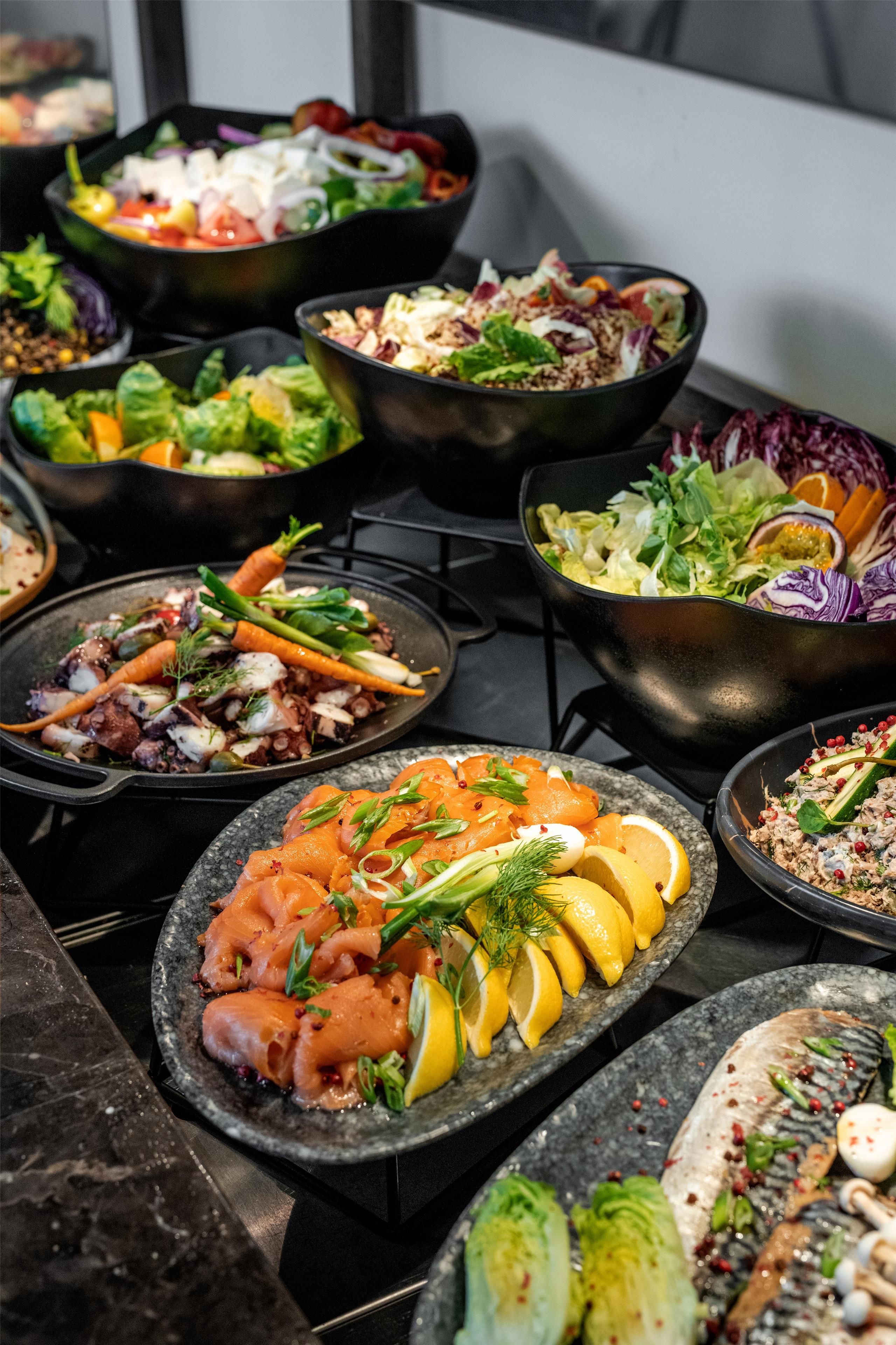 Verschiedene Gerichte, darunter Lachs, Gemüse und Salate, auf einer Küchenarbeitsplatte.
