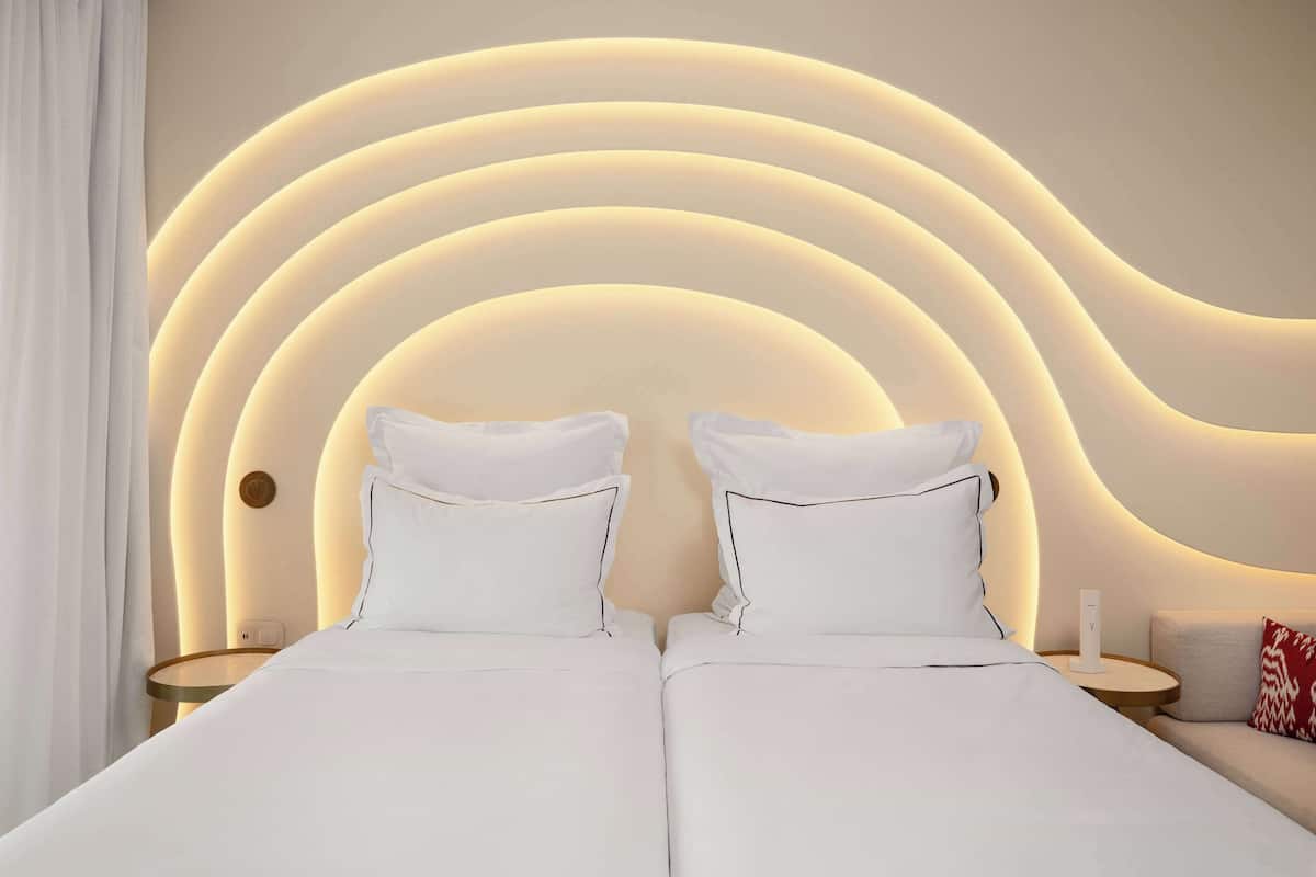 Un lit double avec une literie blanche, une tête de lit moderne ornée de motifs lumineux circulaires et une petite table de chevet avec une lampe blanche.