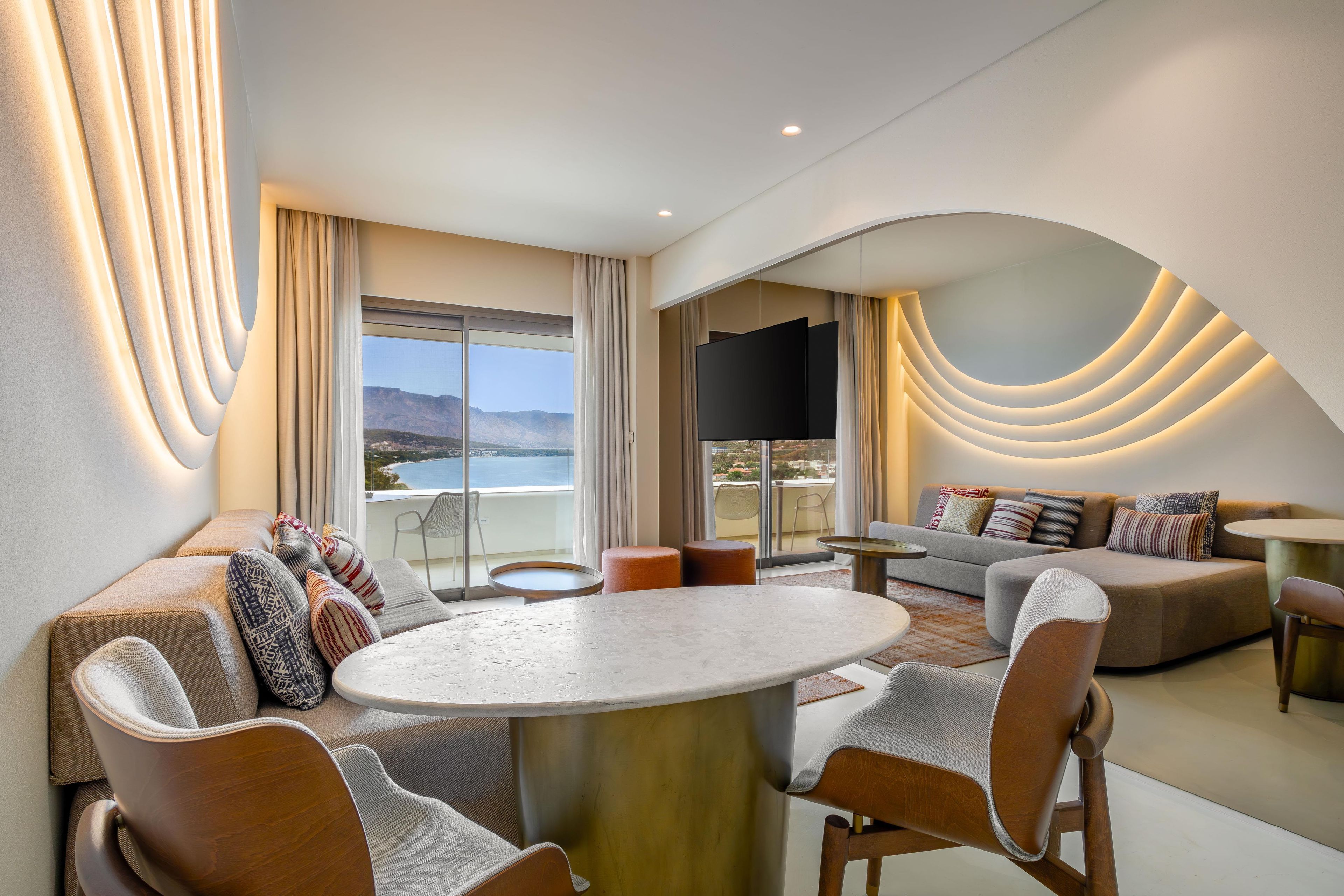 Ein modernes Wohnzimmer mit einem runden Tisch, Sofas und einem großen Fenster mit Bergblick.