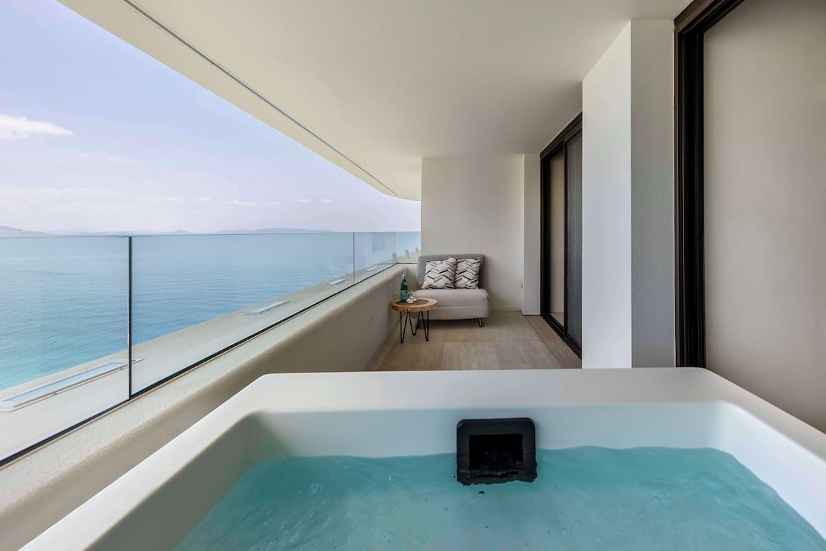 Un balcon avec vue sur la mer, un canapé, une petite table et un jacuzzi.