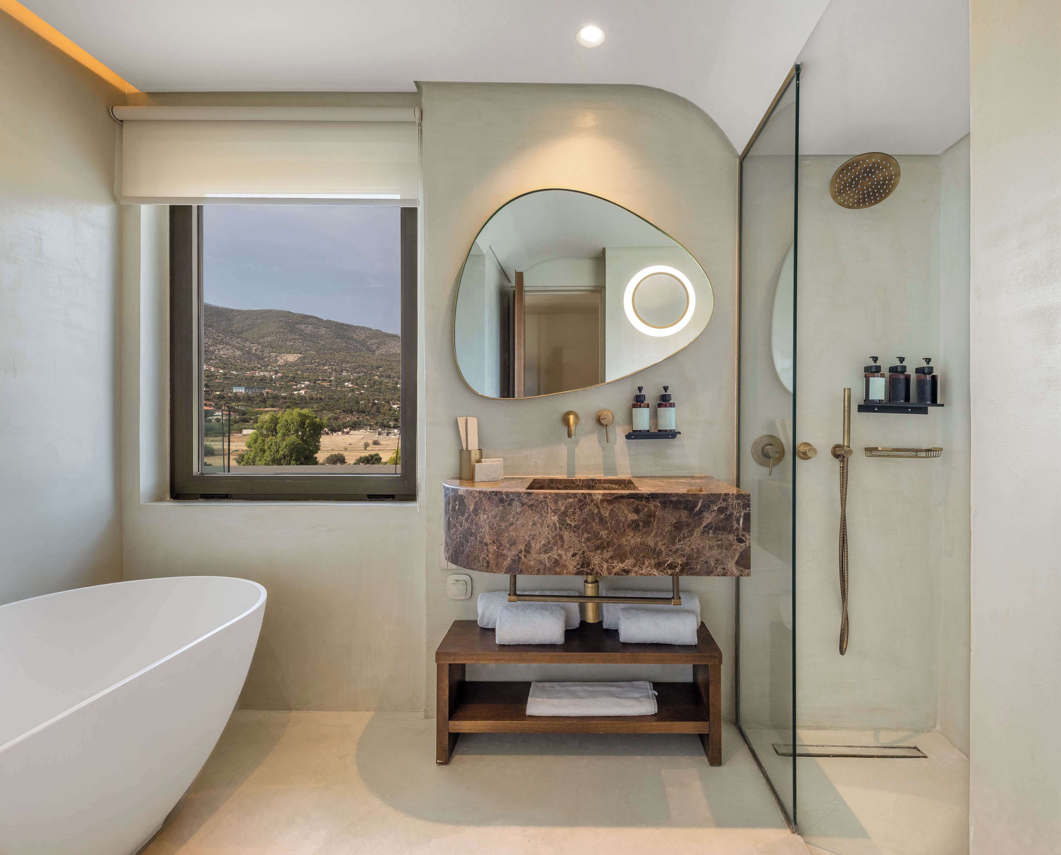 A modern bathroom with a freestanding bathtub, a marble sink, a large mirror with a circular light, and a glass-enclosed shower.