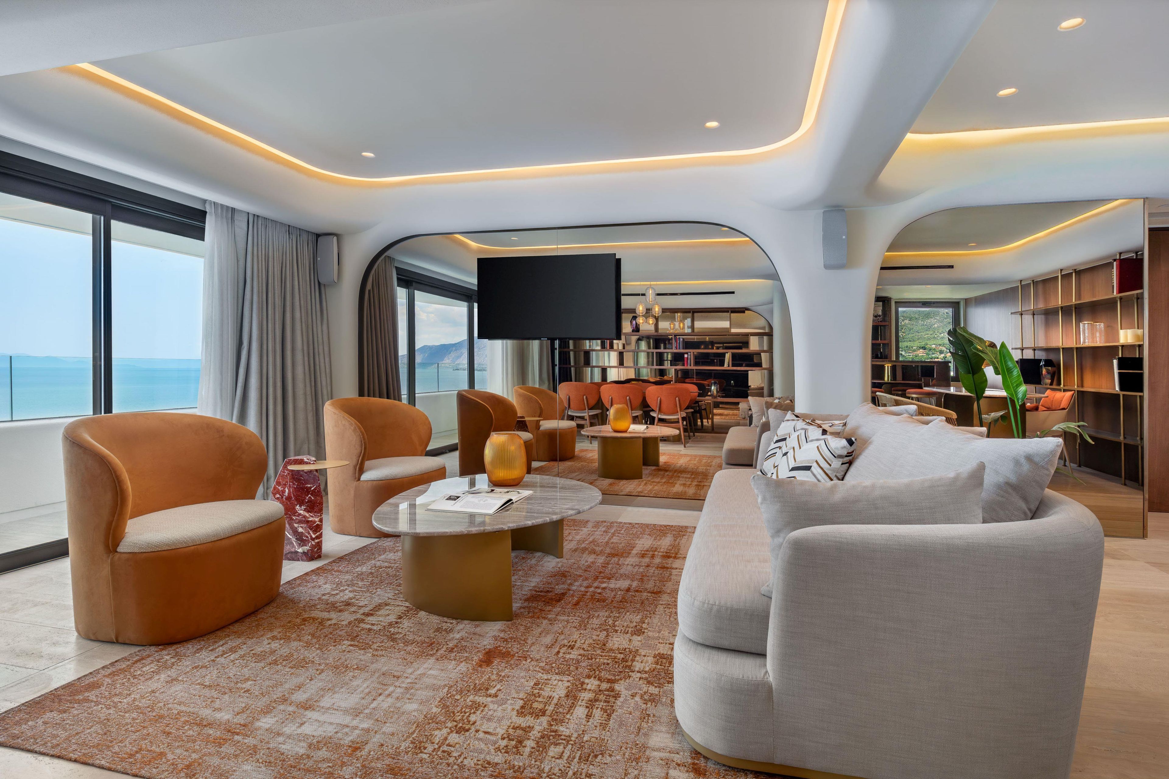 Un salon moderne doté d’un grand téléviseur, de sièges confortables et offrant une vue sur la mer.