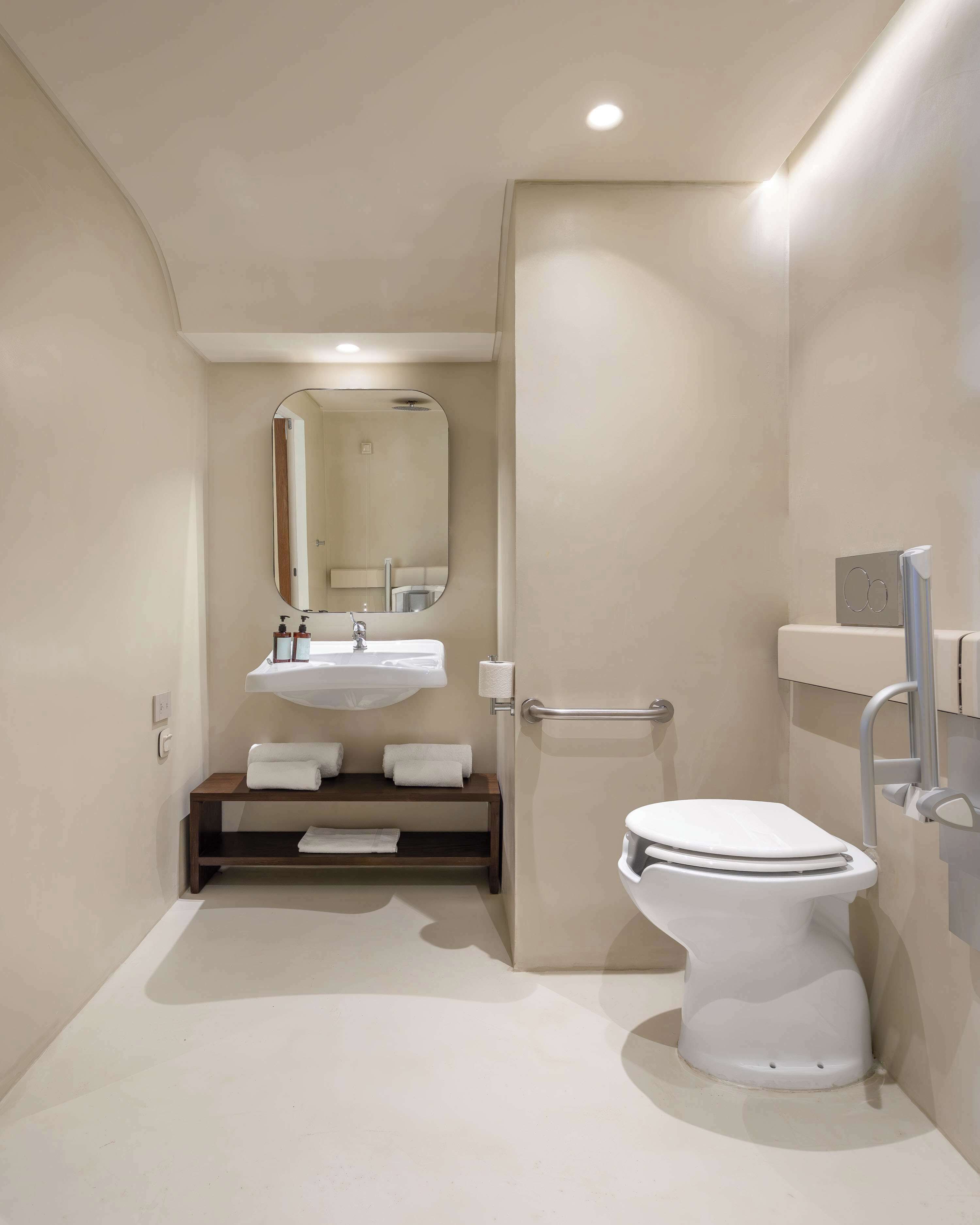 Een moderne badkamer met een witte wastafel, spiegel en toilet. Er is een handdoekrek en een plank met toiletartikelen.