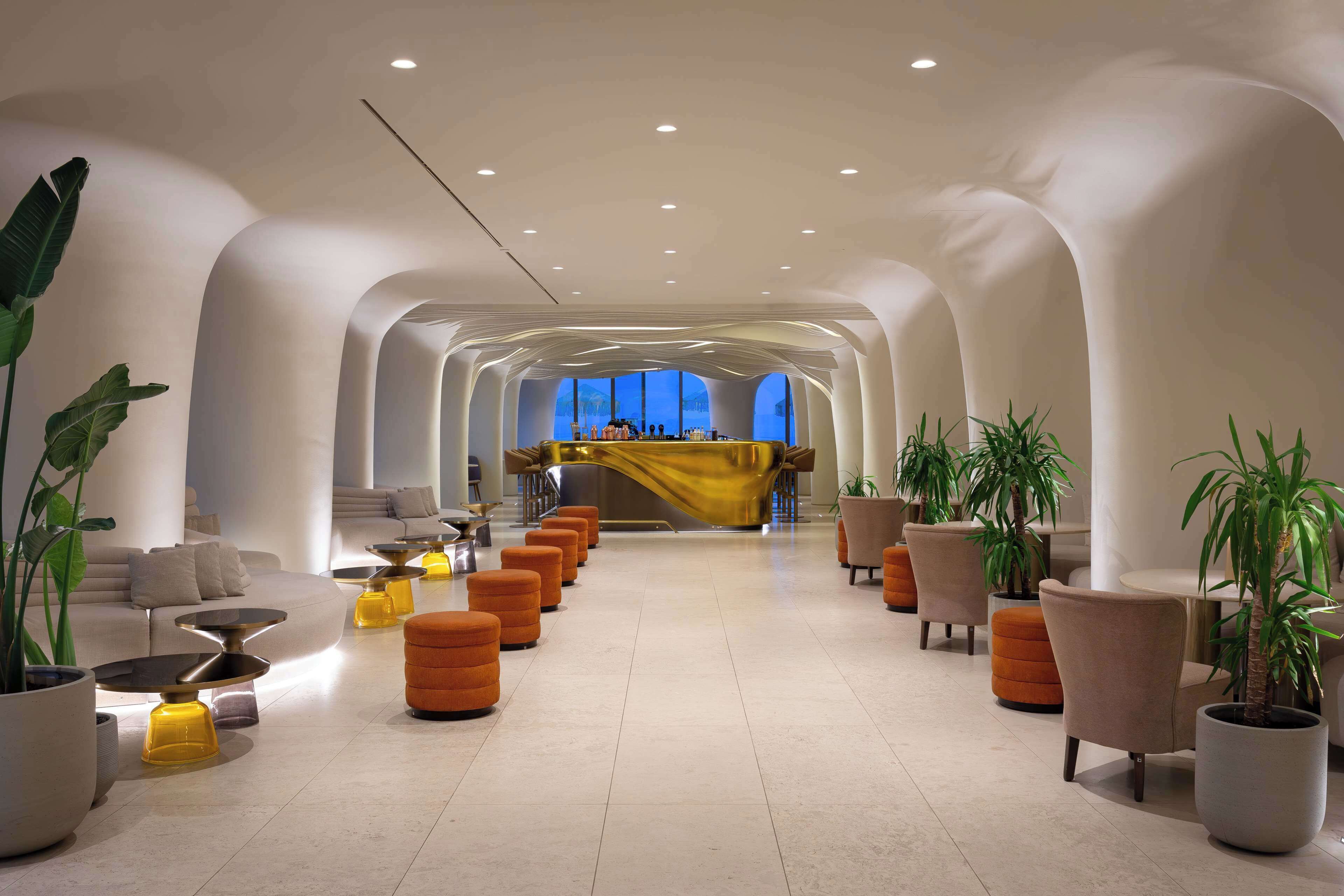 A spacious lobby with a central bar, seating areas, and potted plants.