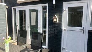 Een terras met een tafel en stoelen, een schuifpui en een witte deur versierd met een huisvormig ornament.