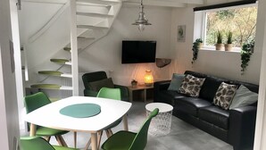 Een moderne woonkamer met een zwarte leren bank, groene fauteuils, een witte tafel en een trap naar een hoger niveau.