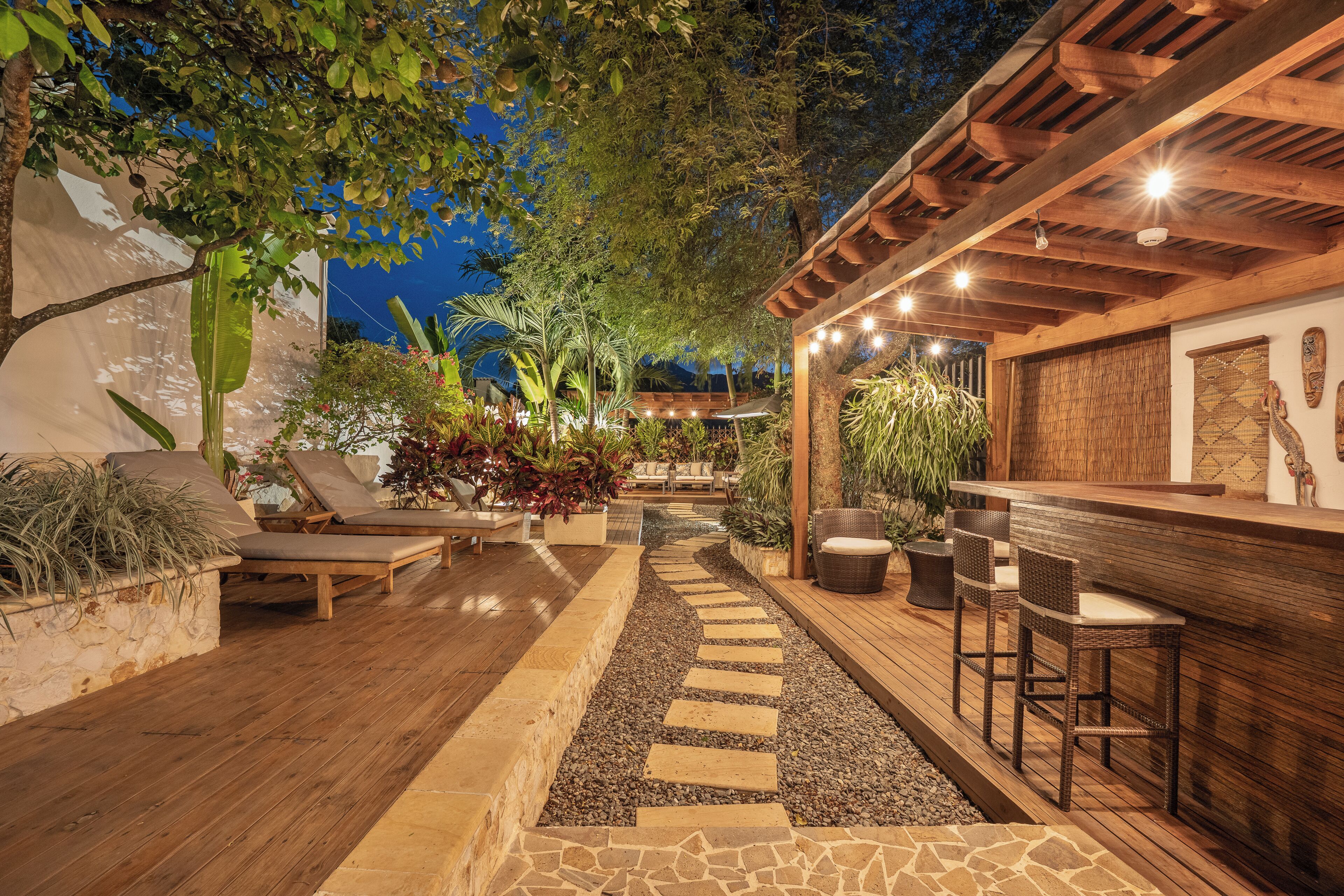 Un patio al aire libre con suelo de madera, escalones de piedra, sillones de descanso y una zona de bar con taburetes.