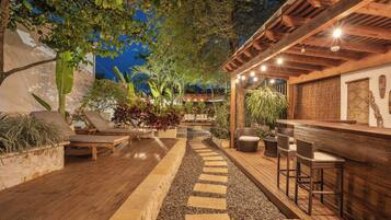 Un patio al aire libre con suelo de madera, escalones de piedra, sillones de descanso y una zona de bar con taburetes.