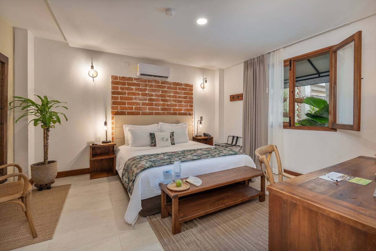 Una camera d'albergo moderna con parete decorata in mattoni, un letto grande, una scrivania in legno e una pianta in vaso.