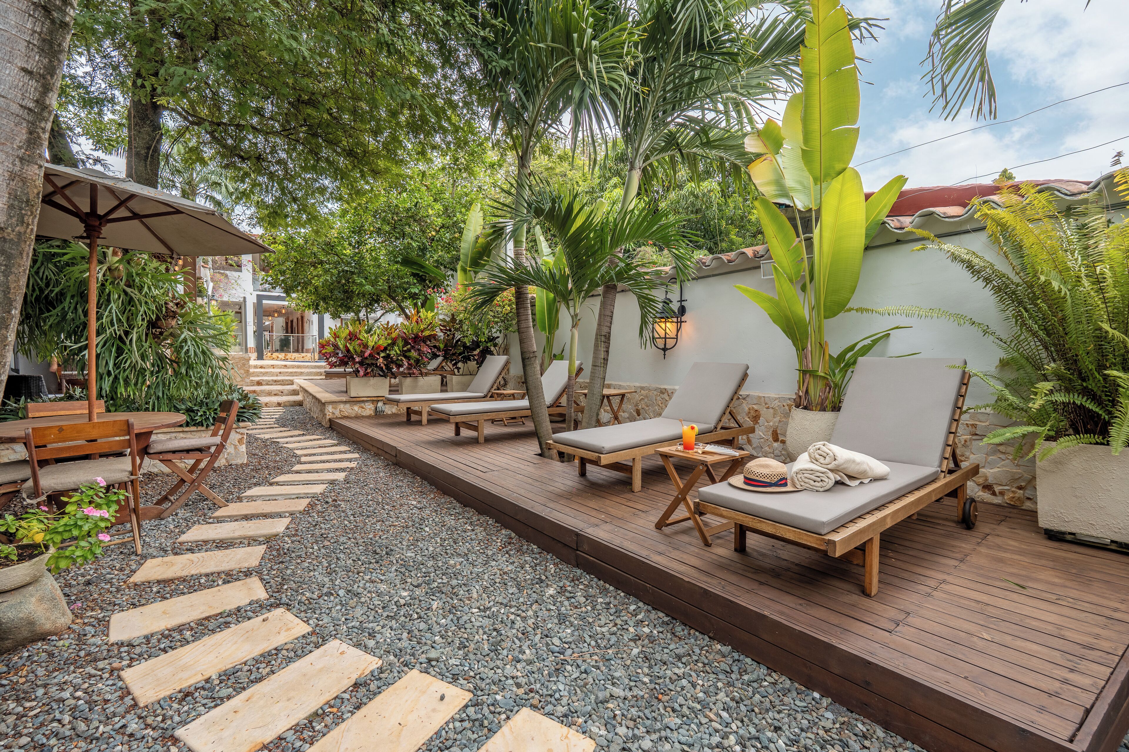 A wooden deck with lounge chairs, a table, and a pathway leading to a covered area with a table and chairs.