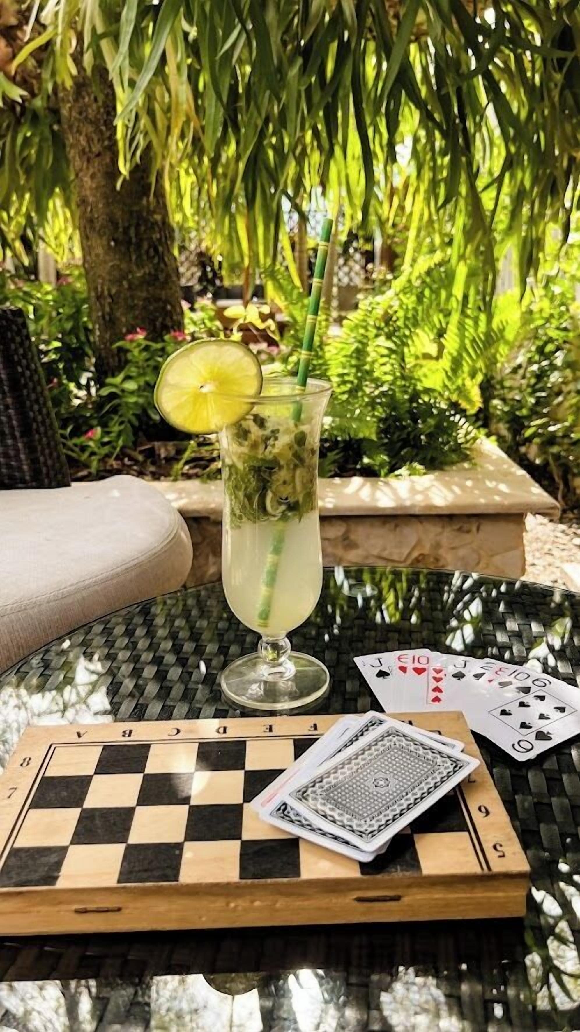 Un verre contenant une boisson, une paille et une tranche de citron vert, posé sur une table avec un jeu d’échecs et un jeu de cartes.