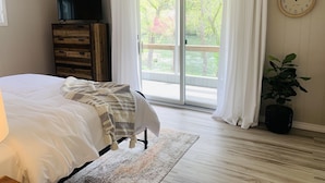 Een slaapkamer met een bed, een dressoir, een televisie, een klok, een raam met gordijnen en een plant.