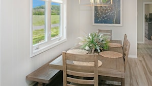 Een eethoek met een houten tafel, geweven placematen en een bloemstuk.